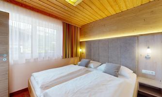 A modern bedroom with two single beds and a warm wooden ceiling. Large windows provide plenty of daylight and a cozy atmosphere.