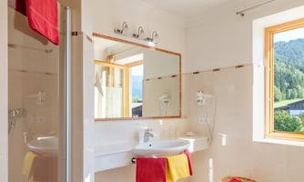A bright bathroom with large windows and a view of the mountains. The decor is modern and adorned with red towels.