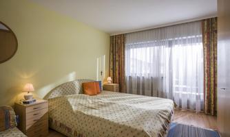A bright bedroom with a large bed and a window that lets in plenty of natural light. The walls are painted in soft colors and there is a cozy atmosphere.