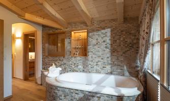 An elegant bathroom with a freestanding bathtub and tiled walls. The room features wooden beams and offers an inviting atmosphere.