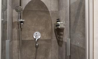 A modern shower with gray tiles. The room is bright and minimally furnished.