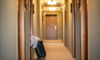 A narrow hotel corridor with several room doors. A suitcase stands against the wall and a cozy atmosphere can be felt.