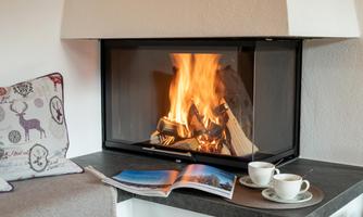 A cozy fireplace with a crackling fire. Next to the fireplace are two mugs and an open book.