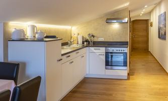 A modern kitchen with wooden flooring and bright walls. It is well equipped with a stove, sink, and countertop.