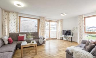 A modern living room with large windows and plenty of natural light. There are comfortable sofas and a table that is decorated.