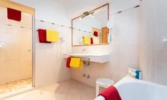 A modern bathroom with a shower and bathtub. Colorful towels hang on the wall and a large mirror reflects the space.