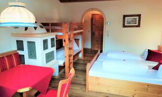 A cozy room with two single beds and a bunk bed. The furnishings are made of wood, featuring a red table and comfortable seating.