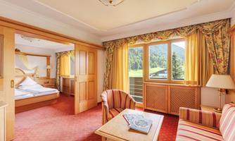 A cozy hotel room with wooden furniture and colorful curtains. Large windows offer a view of nature and provide plenty of daylight.