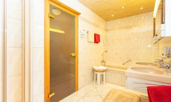 A modern bathroom with tiles and wooden accents. The amenities include a bathtub, a shower, and a washbasin.