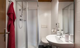 A modern bathroom with a glass shower, a sink, and a large mirror. A red towel hangs on the wall.