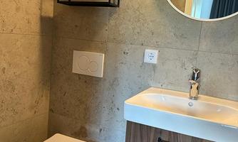 A modern bathroom with an elegant toilet and a small sink. The walls are in neutral tones, and a round mirror complements the design.