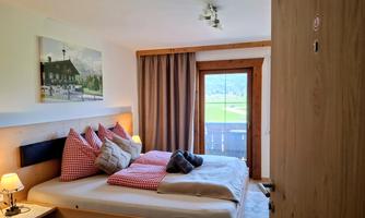 A cozy bedroom with a large bed, decorated with red pillows. In front of the window, you can see a beautiful view of the surrounding landscape.