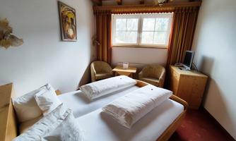 A cozy bedroom with two beds and wooden decor. There is a small table with chairs and a window that lets natural light shine in.