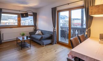 A bright apartment with a cozy living room. The room has large windows, a modern table, and a comfortable couch.