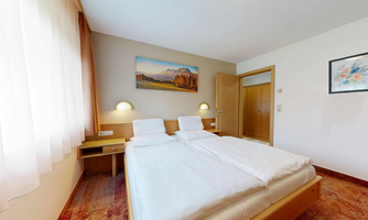 A bright hotel room with two single beds and wooden decor. On the wall hangs a picture and a frame with a plant.