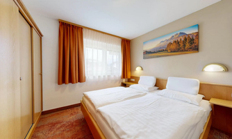 A simple, bright room with two single beds and a large window. A landscape painting hangs on the wall, and the warm curtains give the room a cozy atmosphere.