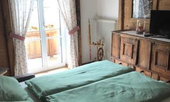 A cozy bedroom with a double bed and green bedspreads. Large windows offer a view of a balcony and provide plenty of natural light.