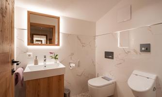 A modern bathroom with clean lines and a bright design. It includes a sink with a wooden cabinet, a toilet, and a mirror with lighting.