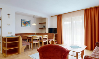 A cozy living space with a dining table and chairs. Large windows provide plenty of daylight and a warm atmosphere.