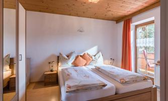 A cozy bedroom with a double bed and warm wooden elements. The window lets in a lot of light and provides access to a balcony.