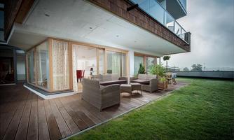 A modern terrace with garden furniture and green lawn area. In the background, large windows and a light-flooded room are visible.