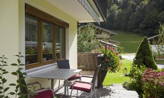 A cozy terrace with a table and chairs. In the background, green meadows and trees can be seen.