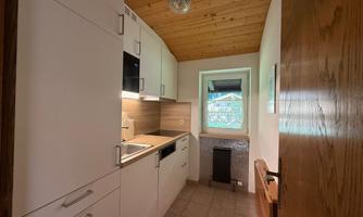 A modern kitchen with white cabinets and a wooden ceiling. There is a window that lets in daylight.