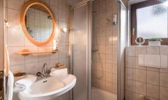 A modern bathroom with a clear shower and a round mirror. The design is bright and friendly, with tiled walls and natural light sources.