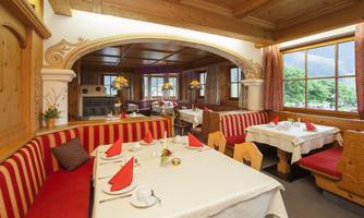 A cozy restaurant with wooden paneling and inviting seating areas. The tables are set with white tablecloths and red napkins.