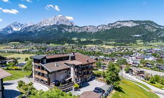 A picturesque landscape with a modern building in the foreground. Majestic mountains rise in the background under a clear blue sky.