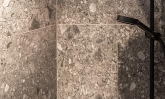 A modern shower with a large, round showerhead and elegant black fixtures. The walls are tiled with a gray stone pattern.