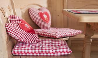 A cozy seating area with checkered heart-shaped cushions and rustic wooden furniture. The cushions are red and give the room an inviting atmosphere.