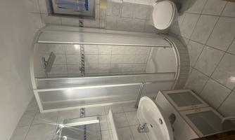A modern bathroom with a shower cabin, a sink, and a toilet. The walls are tiled and there is ample light.