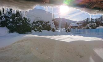 A wintry landscape with plenty of snow and a low-hanging sun. Icicles hang from a canopy.