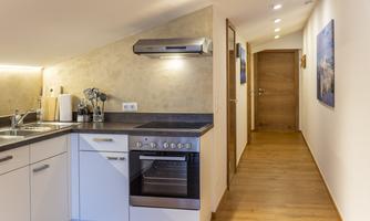 A modern, well-equipped kitchen with a wooden floor and a long hallway in the background. The walls are light and create an inviting atmosphere.