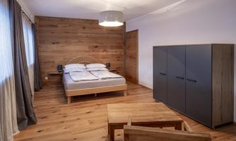 A bright bedroom with a large bed and wood paneling. There is a table and chairs made of wood as well as a modern wardrobe.