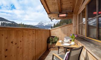 A cozy balcony with wooden paneling and a view of the mountains. On the table are a coffee cup and fresh flowers.