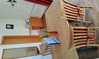 A cozy dining area with a wooden table and four chairs. In the background, a kitchenette and a mirror are visible.