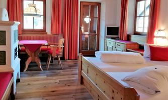 A cozy bedroom with wooden furniture and red curtains. There is a table and chairs as well as a separate seating area.