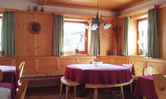 A cozy dining hall with wooden walls and several round tables. The windows are adorned with green curtains, and the decor radiates an inviting atmosphere.
