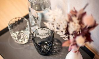 A stylish tray with a water glass, a decorative glass, a key with a wooden heart, and a small vase with dried flowers. The arrangement radiates a cozy atmosphere.