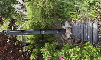 A garden landscape with a black pillar and a wooden pathway. Colorful flowers and green plant growth surround the area.