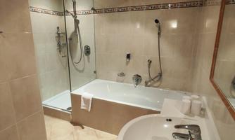 A modern bathroom with a bathtub and a shower. The room has bright tiles and wooden details on the ceiling.
