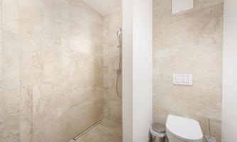 A modern bathroom with a shower cabin and a toilet. The walls are designed with bright, elegant tiles.