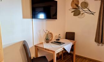A cozy dining area with a table and two chairs. A television is mounted on the wall, and a bottle of water and decorative elements are on the table.