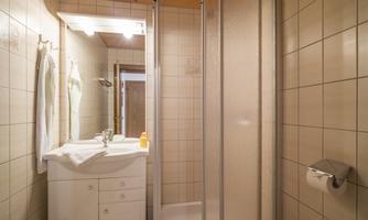 A small bathroom with a shower cabin and a sink. The walls are tiled in light colors and there are towels hanging.