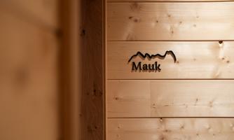 A wooden panel with the inscription "Mauk" and a stylized mountain graphic. The natural wood color adds a warm atmosphere to the room.
