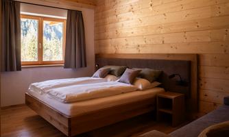 A cozy bedroom with a large bed and wood paneling. The window offers a view of nature.