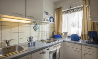 A bright kitchen with modern furniture and appliances. The windows are decorated with yellow curtains, and there are dishes and electrical appliances on the work surface.