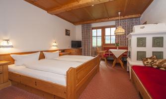A cozy room with wooden furniture, two beds, and a beautiful view from the window. The decor feels warm and inviting, perfect for relaxing stays.